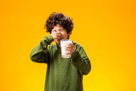 Lactose intolerance. Dairy intolerant unhappy child boy holding glass of milk over yellow background.の写真素材