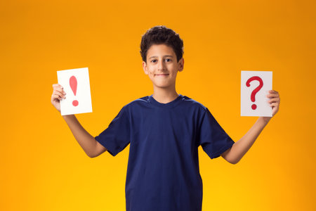 Portrait of kid boy holding question mark and exclamation point card in hand. Education and...