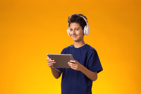 Portrait of child boy using tablet and headphones and playing video game over yellow background. Leisure concept.の写真素材