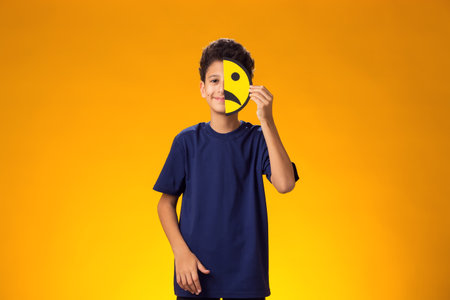 Portrait of child boy holds emoticons on half face with sad emotions.の写真素材