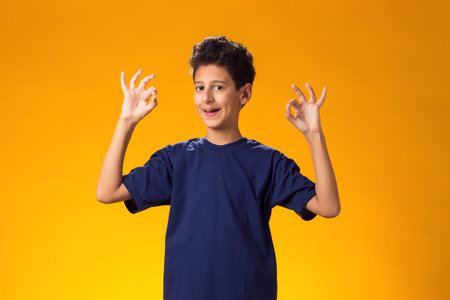 Portrait of smiling child boy showing ok gesture over yellow background. Positive emotions concept