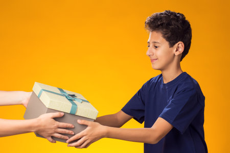 Portrait of child boy receiving giftbox over yellow background. Birthday and celebration conceptの写真素材