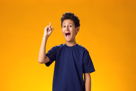 Portrait of smiling kid boy pointing finger up over yellow background.の写真素材
