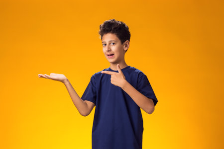 Portrait of smiling child boy pointing finger at something over yellow background. Positive emotions conceptの写真素材