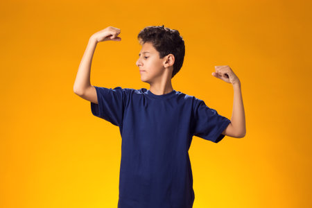 Portrait of kid boy showing winner or strength gesture over yellow background. Success, victory and health conceptの写真素材