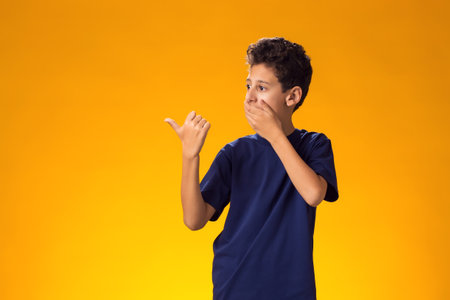 Portrait of kid boy mocking and teasing at someone showing finger at camera over yellow background.の写真素材