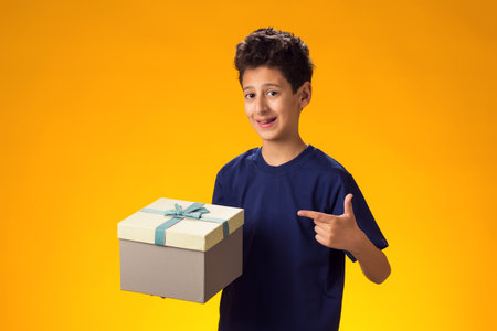 Portrait of child boy holding giftbox and pointing finger at it over yellow background. Birthday and celebration conceptの写真素材