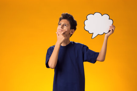 Portrait of thoughtful child boy holding think cloud bubble card and touching cheek with finger....