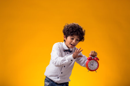 Portrait of child boy holding alarm clock over yellow background. Time management conceptの写真素材