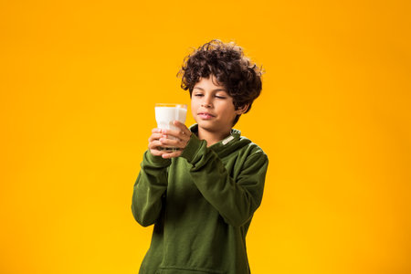 Portrait of smiling child boy holding glass of milk over yellow background. Healthy food conceptの写真素材