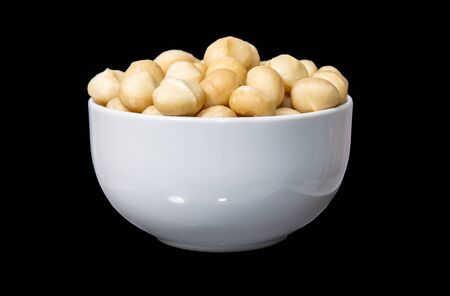 Macadamia nuts in white bowl isolated on blackの写真素材