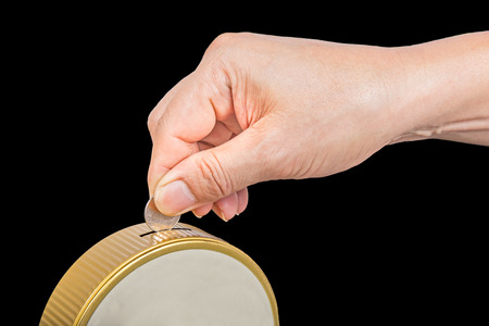 hand put coin into saving box isolated on blackの写真素材