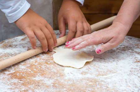 Woman teaches child rolled dough with a rolling pin on the table