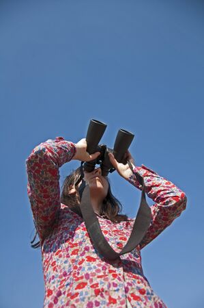 Young woman using binoculars. On blue sky backgroundの写真素材