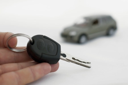 Hand holding keys and a car in the background. White isolatesの写真素材