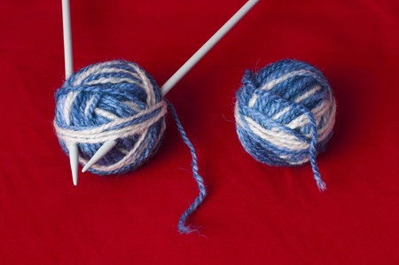 Ball of yarn and knitting skewers. Blue and white color balls on red backgroundの写真素材