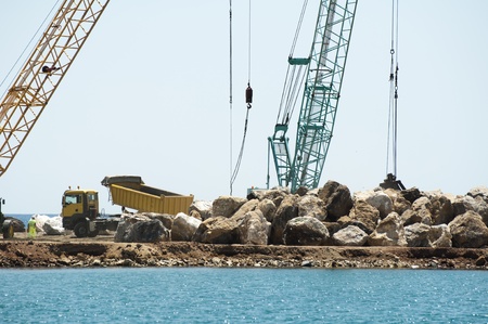 Building a dike. Cranes and excavator put stones in the sea. Trucks carrying stonesの写真素材