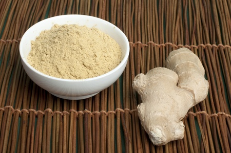 Powdered ginger in a bowl and whole ginger on wooden base
