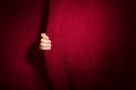 Hand appearing beneath the curtain. Red curtain.の写真素材