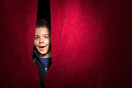 Child appearing beneath the curtain. Red curtain.の写真素材