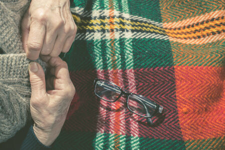 Elderly woman buttoning his vest. Glasses on blanketの写真素材
