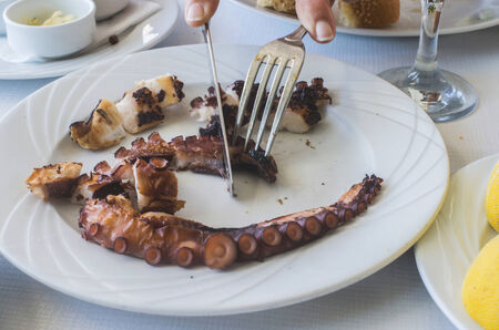 Octopus in a Greek restaurant. Hands are cutting octopus. Greece, Athens, Piraeusの写真素材