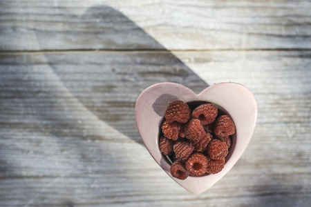 Raspberries in a bowl on wood. Heart shape bowl.の写真素材