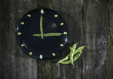 Bean pods and green beans in black plate. Clock conception