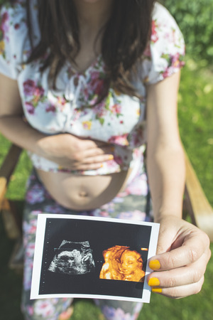 Pregnant women hold picture of womb. Daylight in the gardenの写真素材