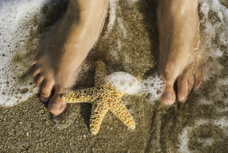 Starfish and feet on the beach. Sea wavesの写真素材