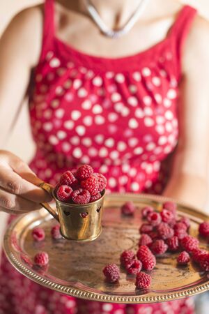 Woman in red dress holding a cup of raspberriesの写真素材