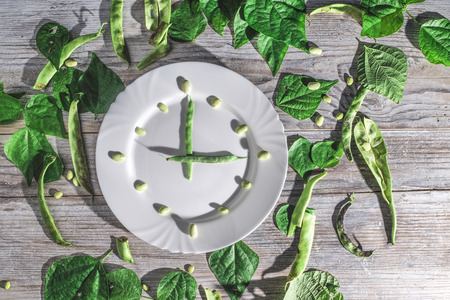 Bean pods and green beans in white plate. Clock conception