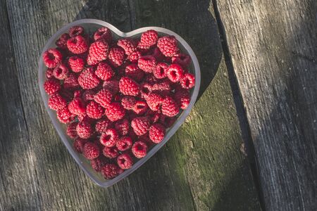 Raspberries in a bowl on wood. Heart shape bowl.の写真素材