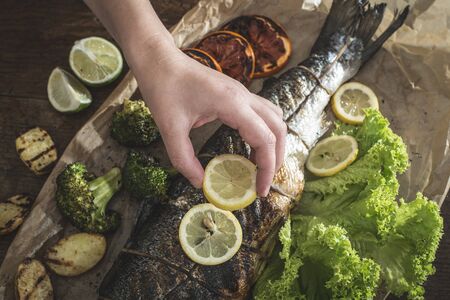 Roasted salmon and vegetables. Hand putting lemon on fishの写真素材