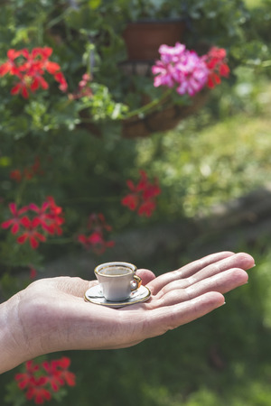 Hand hold very small cup of coffee. Red and pink flower on backgroundの写真素材