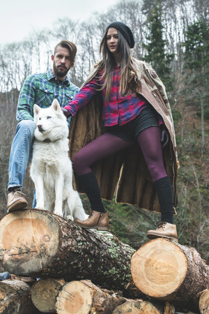 Young woman and men on wood logs in the forest. White dogの写真素材