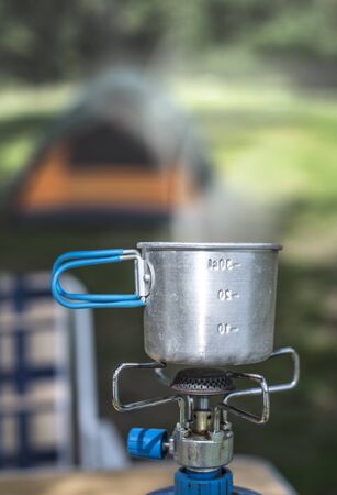Tourist cup on gas stove in the forest. Tent on background.の写真素材