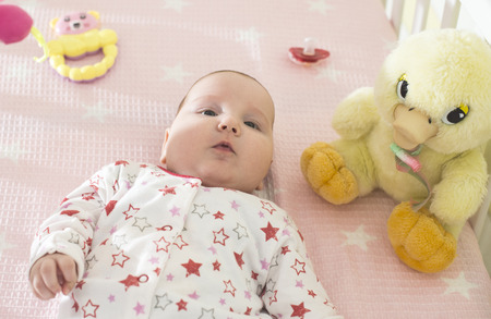 Baby girl in a bed with toys around. Pink tones