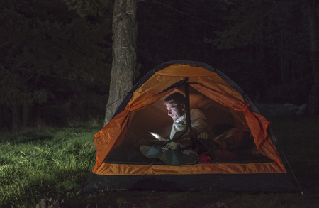 Man watching his smartphone in a tent at night.の写真素材