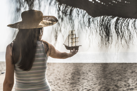Woman with hat hold boat model on the beachの写真素材