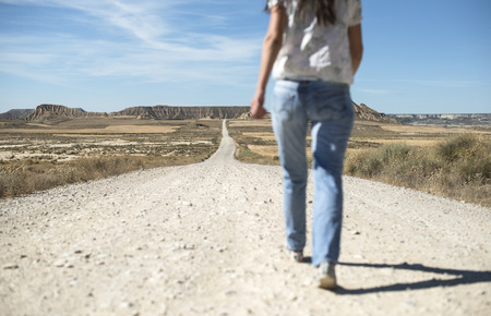 Woman with jeans walking on wild west dirt roadの写真素材