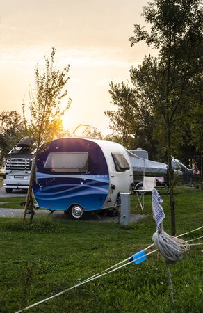 Caravans and campers on green meadow in campsite. Sunrise, rays on campers in the morning. Green...