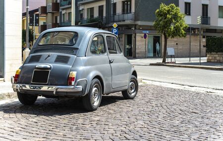 Vintage small car on traditional italian paved street. Dark grey old car.
