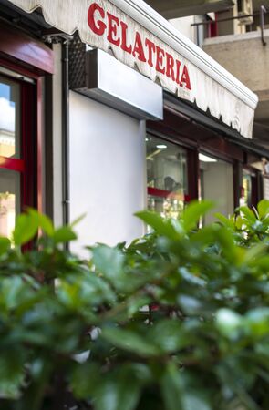 Text gelateria on sunblind. Italian ice cream. Facade on ice cream shop. Green foliage in front of cafe and ice cream shop.の写真素材