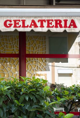 Text gelateria on sunblind. Italian ice cream. Facade on ice cream shop. Green foliage in front of cafe and ice cream shop.の写真素材