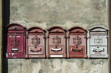 Old vintage mailboxes in Italy. Metal red mailboxes on grey facade. Hard sunlight. Empty plates. Italian house wall. Vintage mail correspondence concept.の写真素材