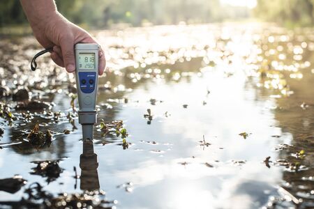 Measure water content with digital device. Sunrise over the water. PH meter.の写真素材