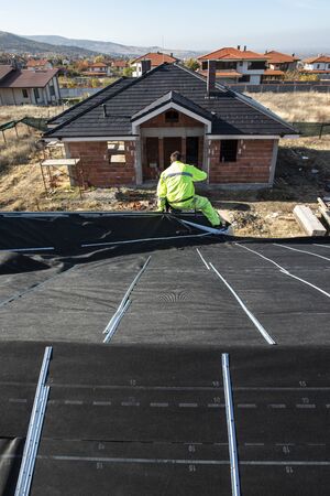 Worker on the top of the house making roof. Building a new house with black roof. Repair and build construction of roof. Conception for roofing, new home, real estate and constructions.の写真素材