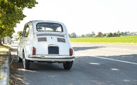 White small vintage car on the street. No people. Asphalt village road in Italy. Travel concept with car.の写真素材