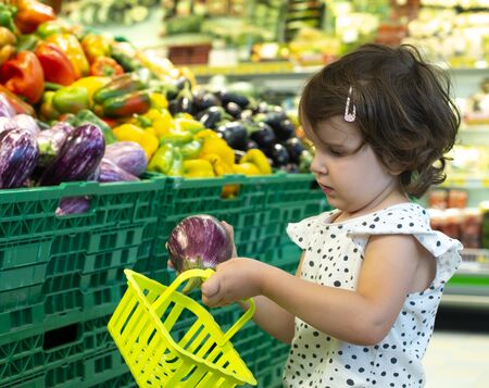 Child shopping eggplants in supermarket. Concept for buying fruits and vegetables in hypermarket. Little girl hold shopping basket.の写真素材